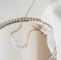 Primo piano della collana minimalista in titanio dorato con otto eleganti perle bianche - Collana