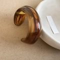 Macro-opname van amberkleurige acryl manchetarmband met bruine marmertextuur en C-vorm - Lichtkoffie