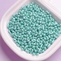 Detailed view of light blue pearlized acrylic peanut beads in a ceramic tray - Cyan