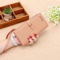 Nude pink long wallet with wrist strap and button closure held by hand in a studio setting - Light Pink
