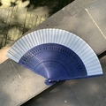 Elegant gradient blue folding fan with intricate carved wood frame on a stone surface - Hollow Fireworks Blue White
