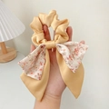 Chouchou en satin beige avec un long ruban à nœud floral rose tenu à la main - Chouchou Nœud Jaune