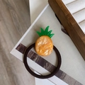 Detailansicht eines glänzenden Ananas-Haargummis mit orangefarbenem Harzanhänger auf Braun - Ananas