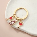 Detailed macro view of gold-tone wine bottle and red enamel cup charms on key ring - Golden Heart Wine Theme
