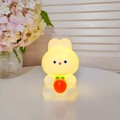 Cute warm yellow glowing rabbit night light holding a red carrot on a white desk - Carrot Rabbit