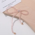 Close-up of pink crystal bow charm with beaded tassels on a rustic wooden background - Pink