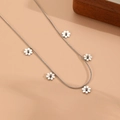 Détail du collier en chaîne argentée avec cinq pendentifs fleurs délicats sur fond beige - Collier Marguerite Couleur Acier