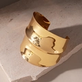 Primer plano de brazalete abierto ondulado ancho con acabado dorado sobre piedra - Dorado
