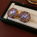 Dettaglio di orecchini vintage con cristallo viola quadrato e strass colorati su fondo beige - Orecchini a Bottone Quadrati Stile Palazzo Viola (Perno S925 N.1)