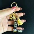 Detail of black resin letter L keychain with dried flowers, gold bee and yellow tassel - Letter L