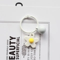 Close-up of a white daisy keychain with a matching bell on a minimalist paper background - White