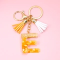 Detail of resin letter E keychain with embedded corn kernels, gold foil, and tassels - Letter E