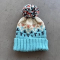 Close-up of winter knit beanie featuring geometric jacquard pattern and large pompom - One Size / Lake Blue