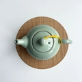 Green celadon teapot with ice crackle glaze on brown bamboo mat, top view - Carbonized Round 15cm