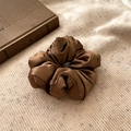 Detail of a brown satin scrunchie with glossy texture on a beige knitted fabric - Coffee