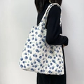 Bolso tote de lona con estampado de arándanos llevado por modelo sobre pared blanca - Caqui Azul Púrpura