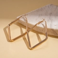 Close-up of golden geometric rhombus earrings displayed on white marble stone base - Large / Gold