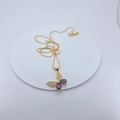 Macro-opname van de vergulde vlinderhanger met paarse stenen op witte basis - Ketting met Hanger / Paarse Vlinder