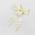 Detail view of a cream satin bow hair clip with elegant pearl embellishments on ribbons - Beige