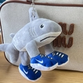 Close-up of a shark plush keychain in grey wearing blue sneakers on a beige canvas bag - 16cm Three-legged Shark