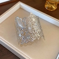 Detailed shot of a silver hollow floral pattern cuff bracelet on a jewelry display tray - Hollow Flower Bracelet / Bracelet - Silver