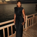 Sleeveless black maxi dress with waist knot detail worn by a model on a sunset seaside balcony - Black