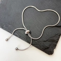 Detail eines silbernen Schlangenarmbands mit verstellbarem Verschluss auf dunklem Stein - Schleife Armband / Silber