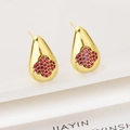 Macro shot of gold teardrop earrings with red clover zircon inlay on a white platform - Red