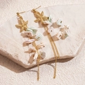 Detailed view of starfish earrings with natural shells and gold chains on stone - Gold