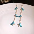 Détail de boucles d'oreilles dorées à pompons avec pierres bleues sur assiette blanche - 34# Crochet d'oreille-Or-Bleu