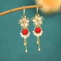 Detalle de pendientes dorados con borlas, cuentas rojas y circón en soporte de metal - Borla de Flor Roja Dorada