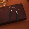 Detailansicht der kleinen matt schwarzen Feder-Ohrhänger auf einer Vintage-Schmuckschatulle - Schwarz