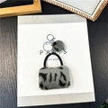 Detail eines Schlüsselanhängers mit Leopard-Plüschtasche, grauem Pompon und Silberclip - Grau