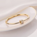 Elegant gold titanium steel bracelet with sparkling diamond cylinders on a white porcelain dish - Gold