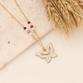 Golden butterfly necklace with colorful beads on a minimalist stone display - Butterfly