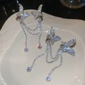 Clip d'oreille papillon argenté avec glands et strass brillants sur assiette beige - Clips d'Oreilles Argentées (Paire)