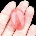 Oval strawberry quartz gemstone for DIY jewelry making held against black background - Watermelon Red (Synthetic)