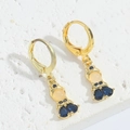 Detail eines goldenen Puppenohrrings mit blauem Zirkon auf weißem Steinuntergrund - Gold Humanoid Mit Blauem Zirkon