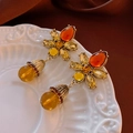 Macro detail of vintage floral earrings with orange gemstones on a white relief plate - Golden Flower Amber Drop (S925 Pin)