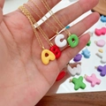 Collane a maglie dorate con pendenti colorati a forma di lettere in resina su una mano - Lettera A