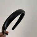 Detail view of a classic black padded headband with a smooth finish held by hand - Narrow Style / Black