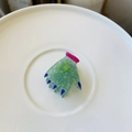 Macro view of green glitter acetate hand-shaped hair clip on a white ceramic plate - Mini Devil Hand