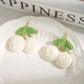 Detail of handmade bohemian white cherry earrings with green leaves on ceramic plate - White