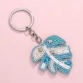 Blue and white beaded monstera leaf keychain with sequins and silver chain on pink background - Blue With Leaves