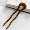 Detail of tortoise shell acetate U-shaped hair pin on white cloth next to a book - Amber Brown