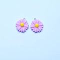 Detail of two purple resin daisy charms with yellow centers and silver hooks for jewelry - Violet