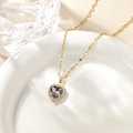 Macro detail of heart-shaped necklace with grey gemstone and gold chain on ceramic plate - November - Dark Grey