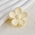 Vue détaillée d'une pince à cheveux mate en forme de fleur jaune sur surface texturée - Blanc Cassé