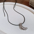 Détail d'un collier pendentif croissant argenté avec cordon noir sur plateau blanc - Collier-Noir-Argent
