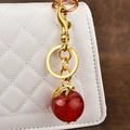 Red glitter apple keychain with golden leaf hanging on a white quilted luxury handbag - Glitter Red